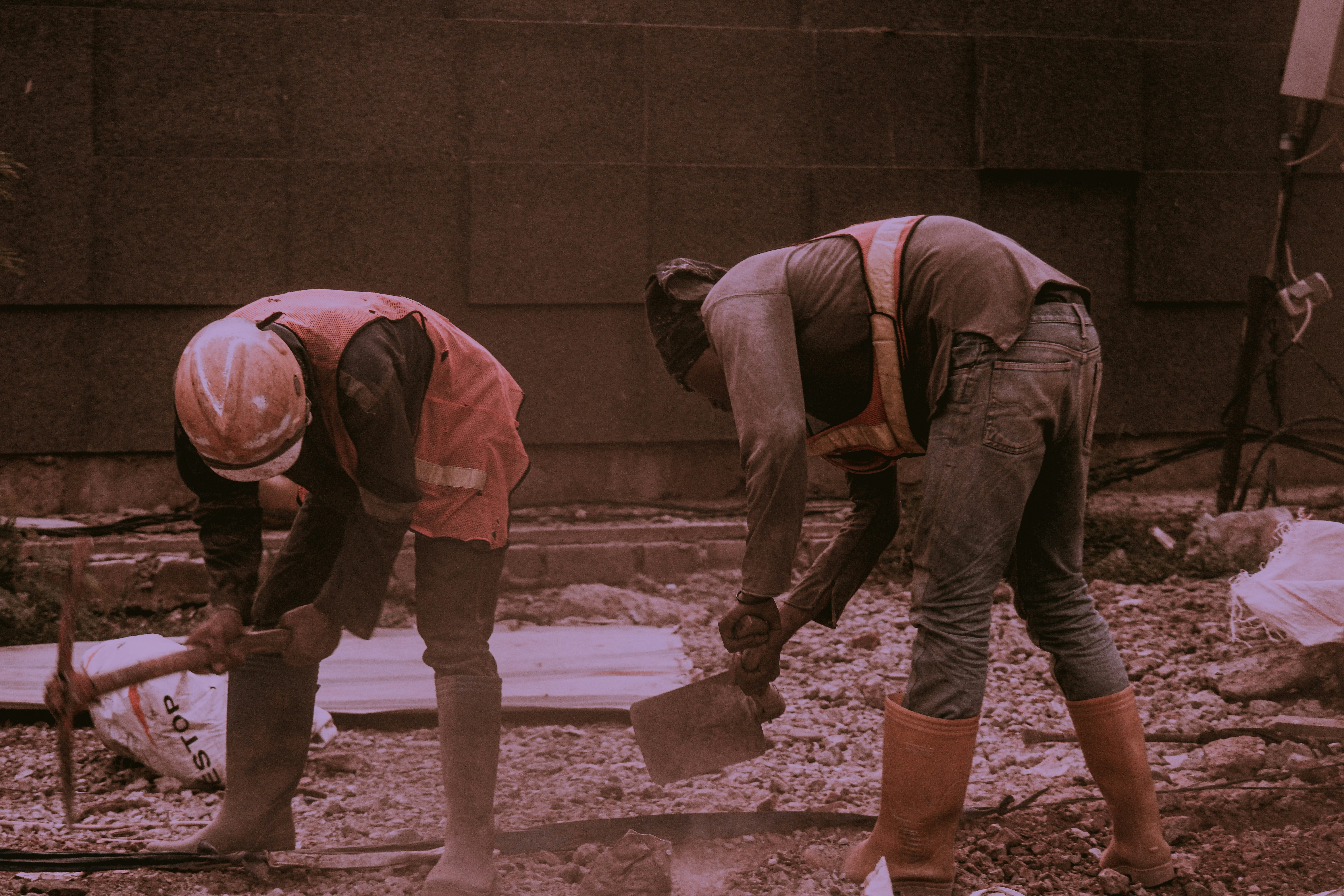 建設現場でヘルメットを被り、汗だくで石膏ボードを担いでいる作業員の男性